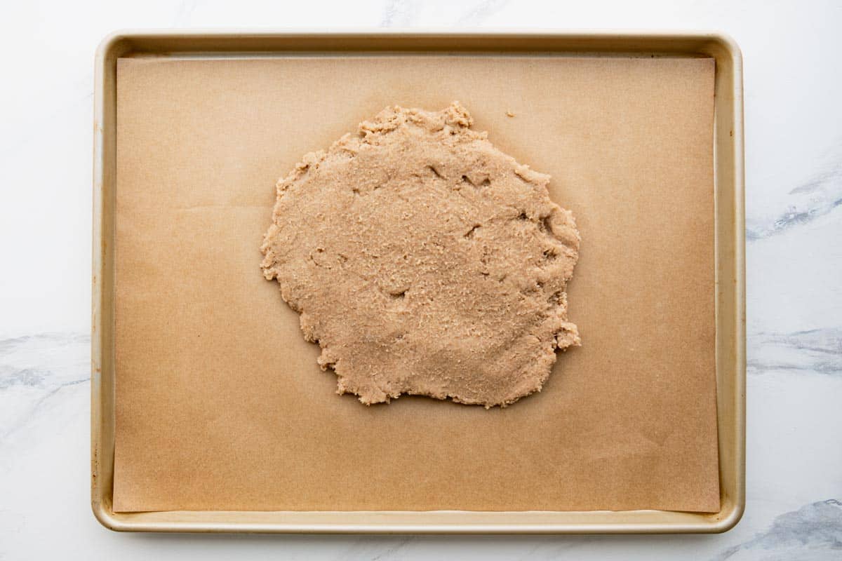 Dough for pecan bars on a parchment lined baking sheet.