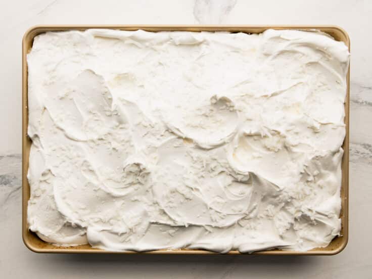 Adding Cool Whip and coconut to the top of the cake.