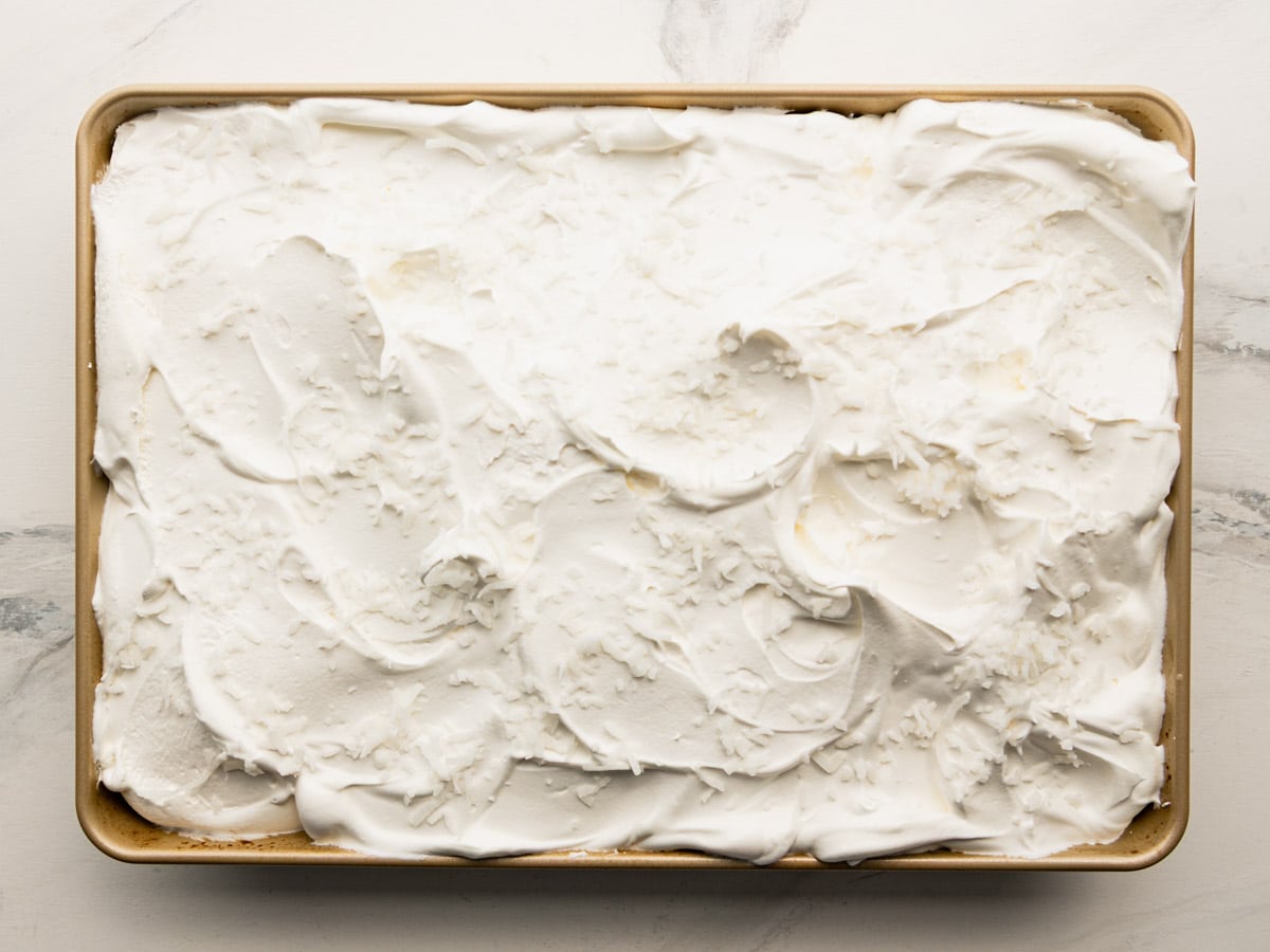 Adding Cool Whip and coconut to the top of the cake.