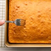 Poking holes in the top of the cake with a fork.