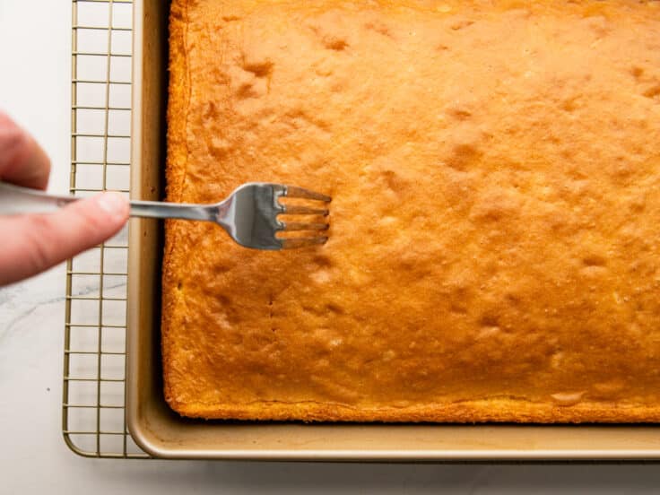 Poking holes in the top of the cake with a fork.