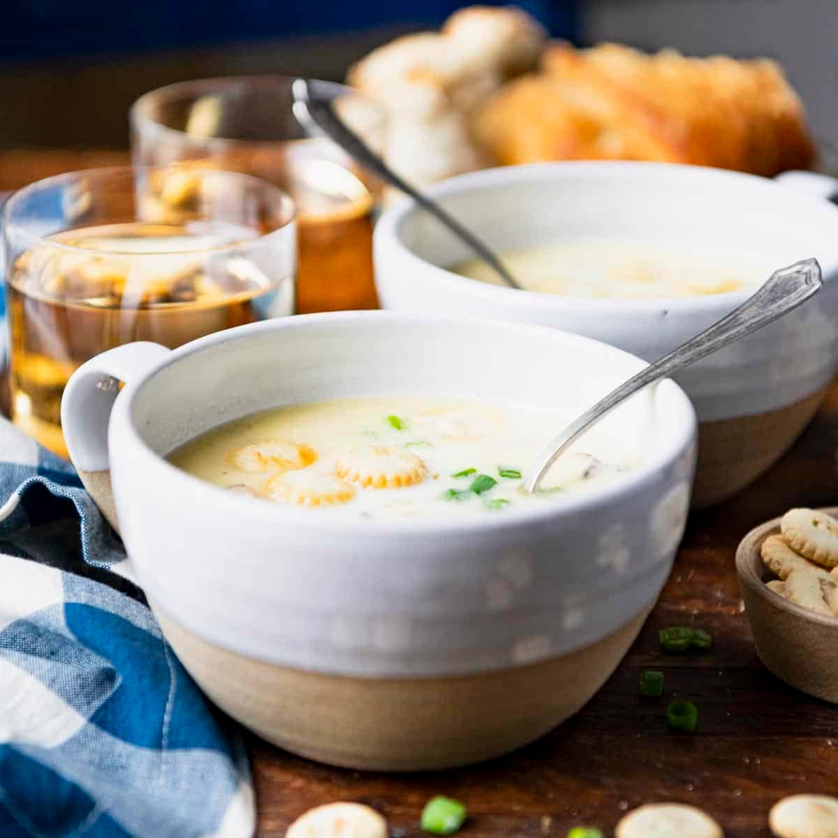 Square side shot of oyster stew served with wine and bread on a dinner table.