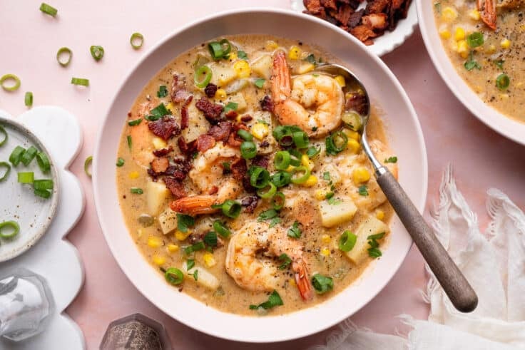 Horizontal overhead shot of a bowl of shrimp and corn chowder garnished with crispy bacon and sliced green onions.