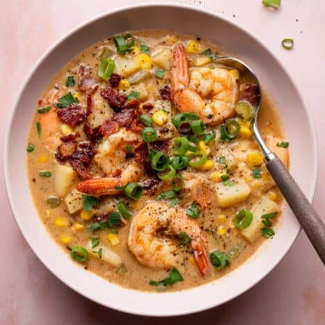 Square shot of a bowl of shrimp and corn chowder garnished with crispy bacon and sliced green onions.