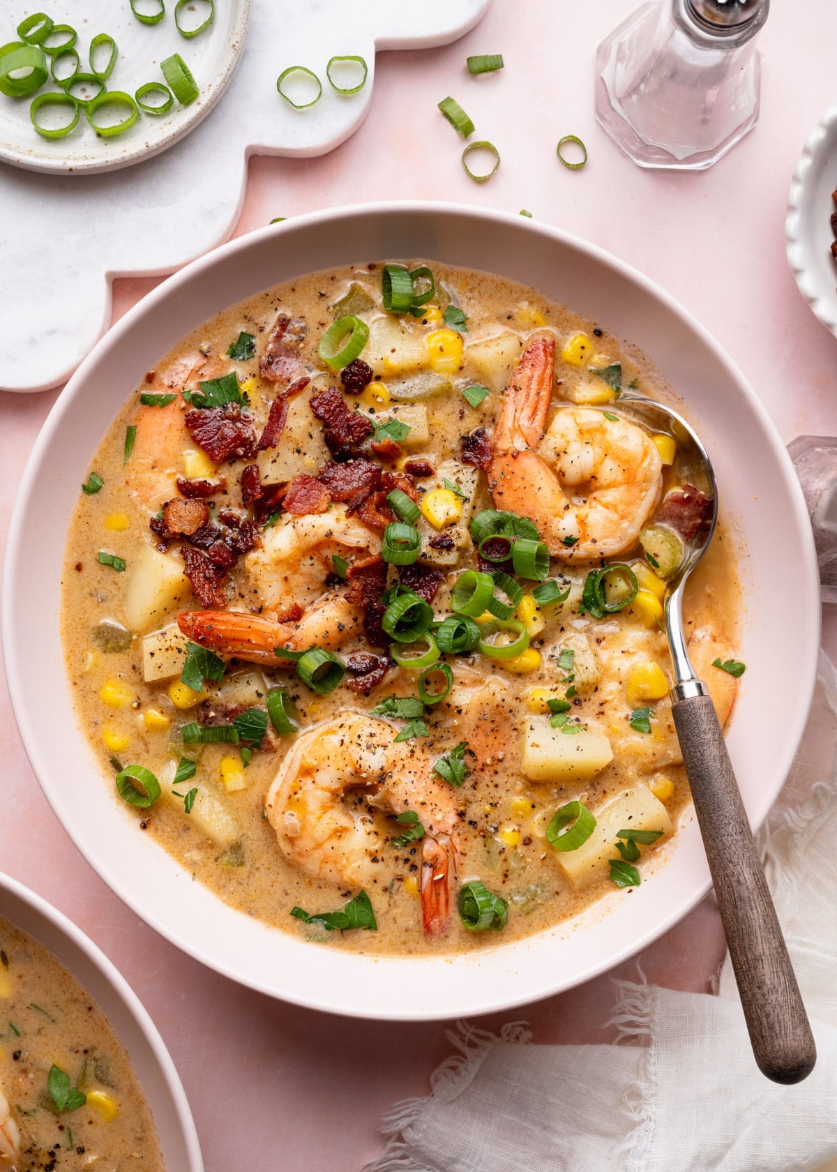 Overhead shot of a bowl of shrimp and corn chowder garnished with crispy bacon and sliced green onions.
