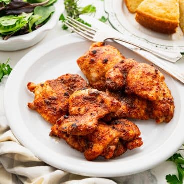 Square side shot of baked chicken thighs on a white plate.
