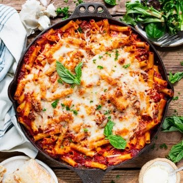 Square overhead shot of baked ziti with sausage and fresh basil garnish on top.