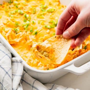 Square side shot of a hand using a tortilla chip to scoop up an easy buffalo chicken dip recipe.