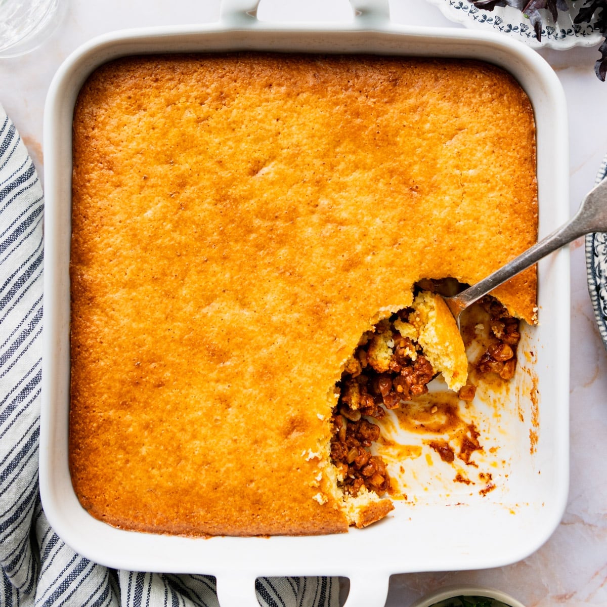 Square overhead image of a white baking dish full of cornbread casserole with ground beef.