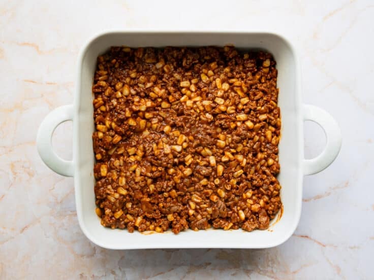 Spreading the ground beef filling in the bottom of a square white baking dish.
