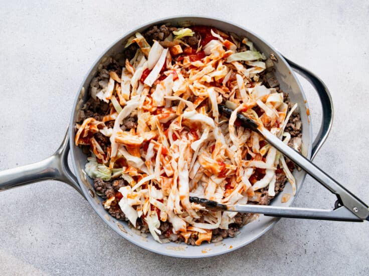 Adding the cabbage, tomatoes, and sauce to the skillet.