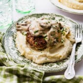 Horizontal side image of hamburger steak with gravy on a green and white plate served with mashed potatoes.