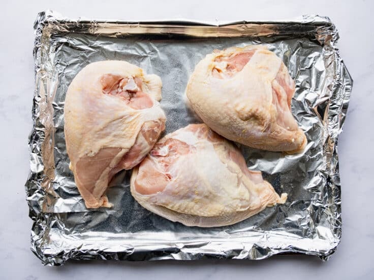 Bone in skin on chicken breast on a foil lined rimmed sheet pan.