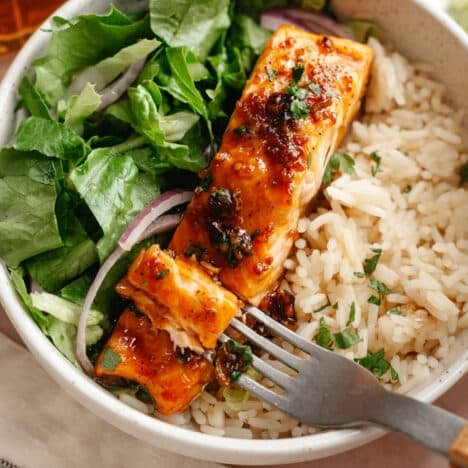 Square side shot of a bowl of bourbon glazed salmon with rice and salad greens.