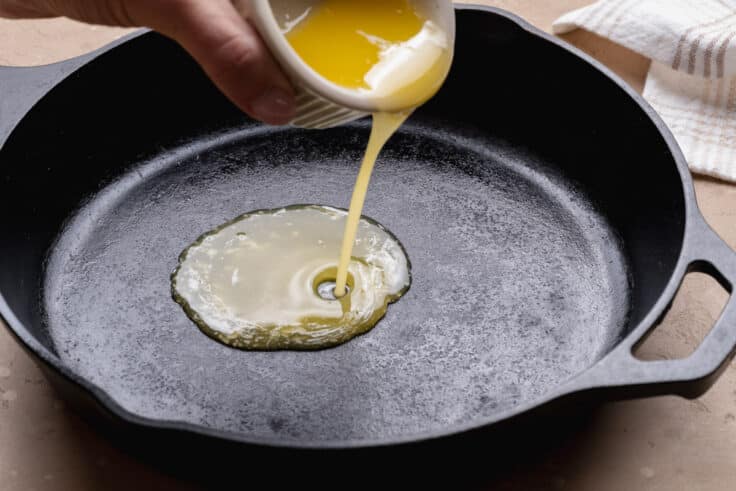 Pouring melted butter into a cast iron skillet.