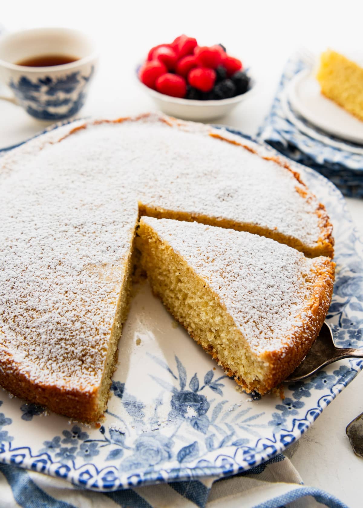 Sliced breakfast cake dusted with powdered sugar and served on a blue and white platter.