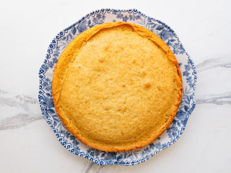 Overhead shot of a baked breakfast cake on a serving plate before slicing.