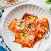 Close overhead shot of a plate of baked ravioli with fresh parsley on top.