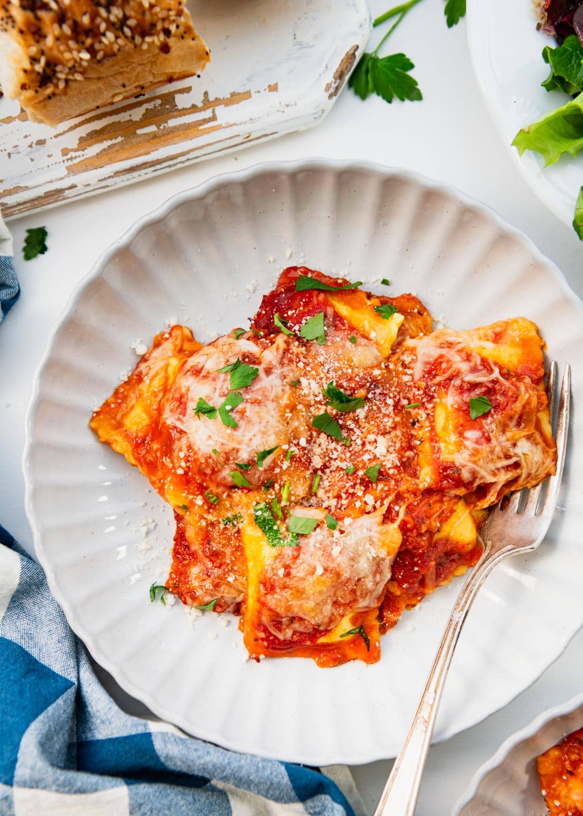 Close overhead shot of a plate of baked ravioli with fresh parsley on top.