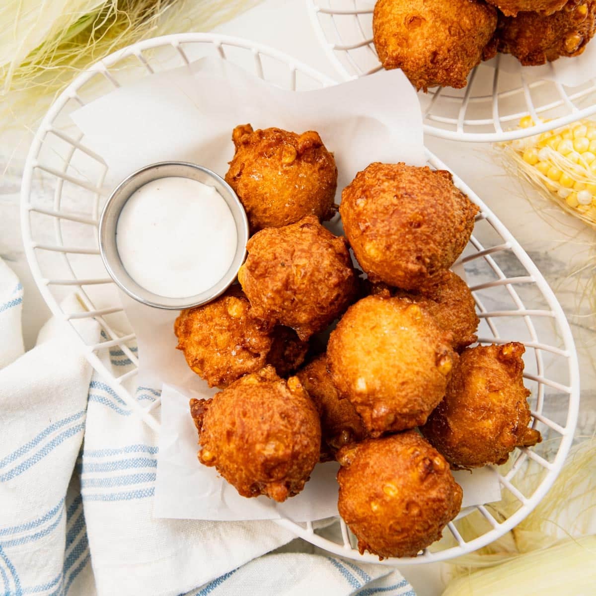 Square overhead shot of the best corn fritters recipe in a basket with a side of ranch for dipping.