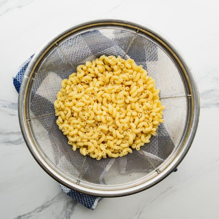 Boiled elbow pasta draining in a colander.