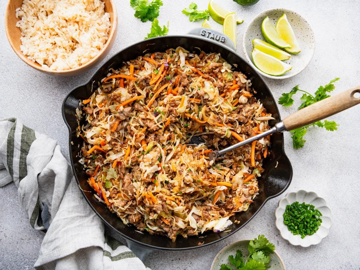 Horizontal overhead shot of an eggroll in a bowl recipe on a white table with a side of rice.