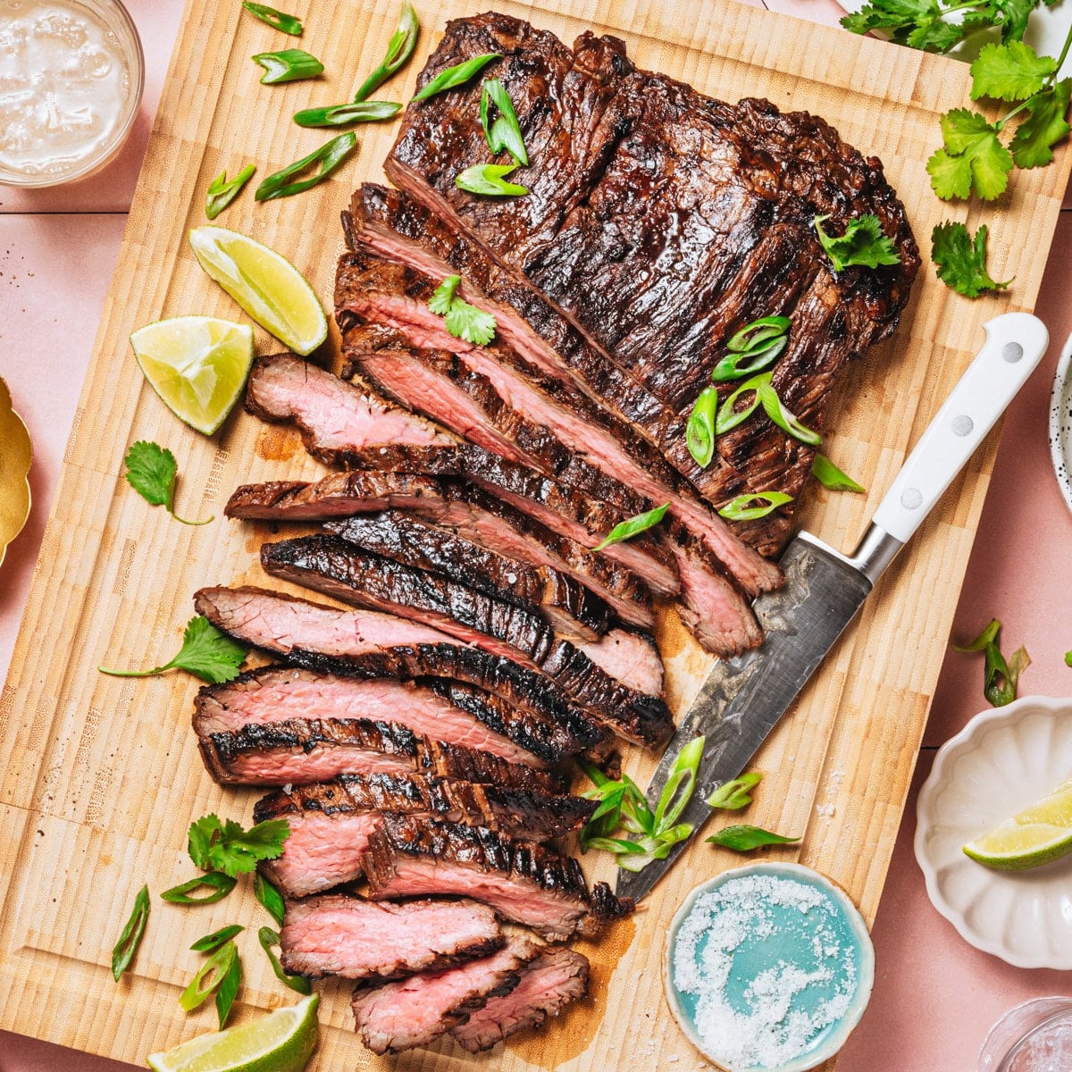 Square overhead shot of sliced marinated grilled flank steak on a wooden cutting board.