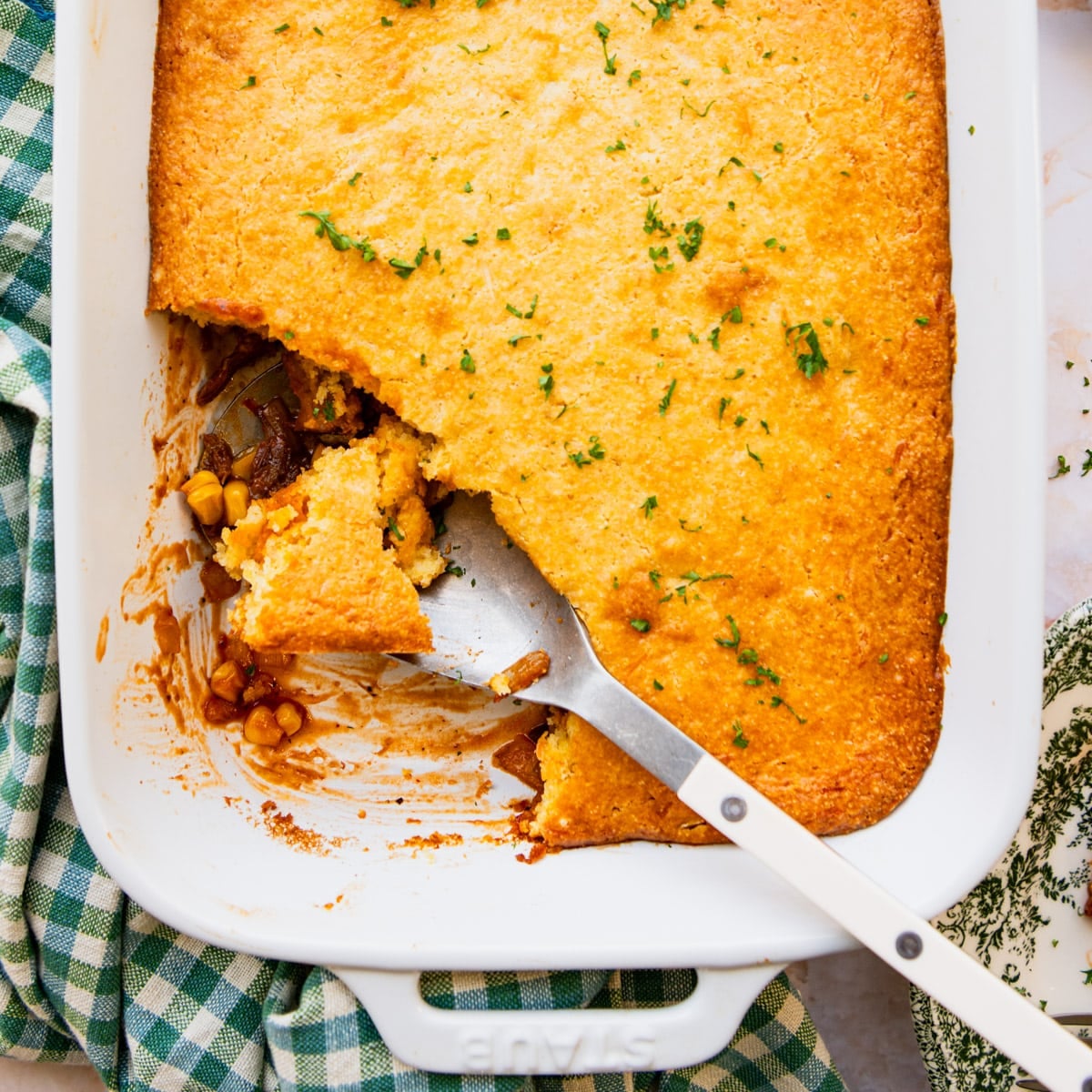 Square overhead shot of a pulled pork casserole with a cornbread crust in a white baking dish.