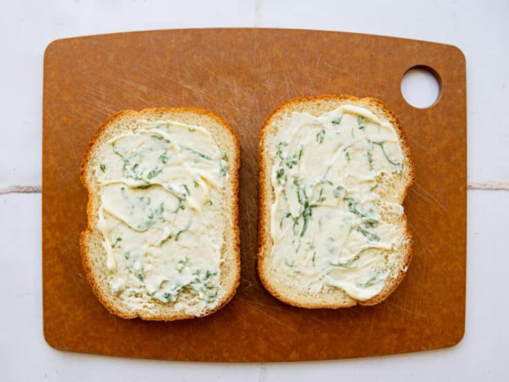 Spreading basil mayo on two slices of white bread.