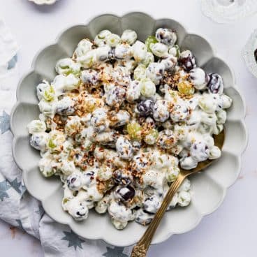 Square overhead shot of a bowl of grape salad on a white marble table.