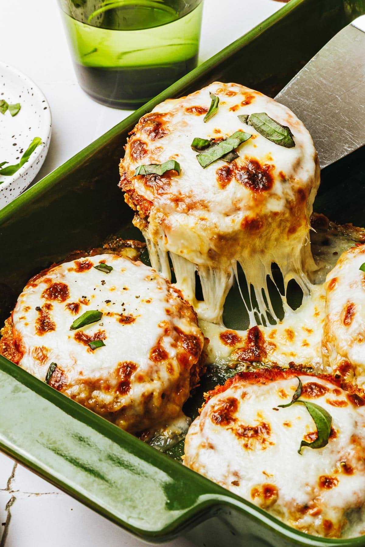 Side shot of baked eggplant parmesan in a green baking dish.