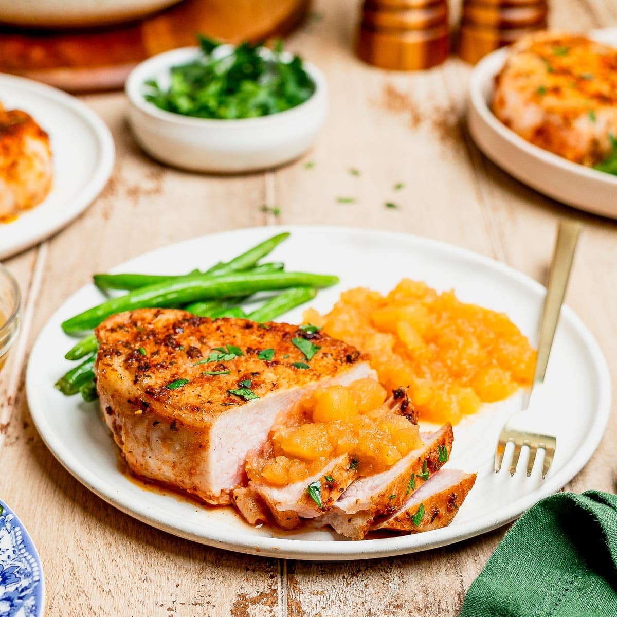 Pork chops and applesauce served on a white plate on a dinner table.