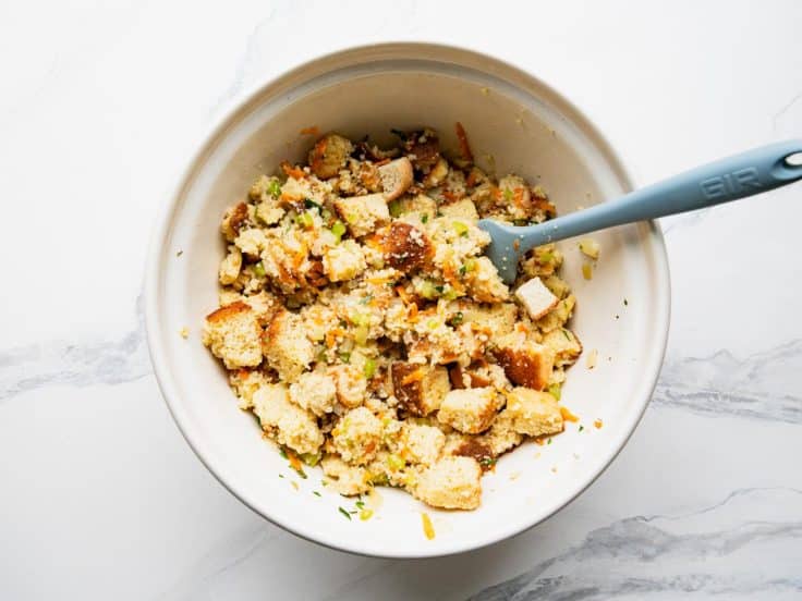 Process shot showing how to make cornbread dressing in a white mixing bowl.