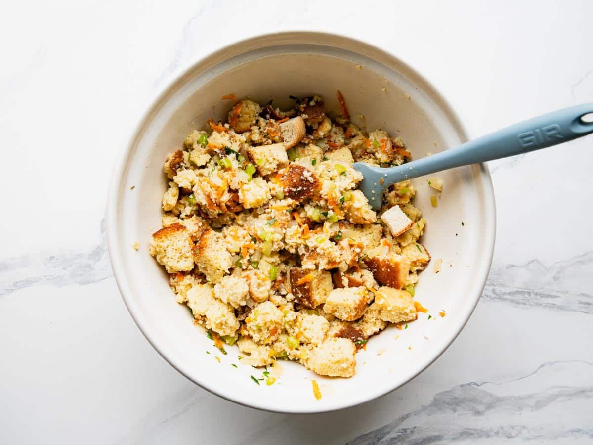 Process shot showing how to make cornbread dressing in a white mixing bowl.