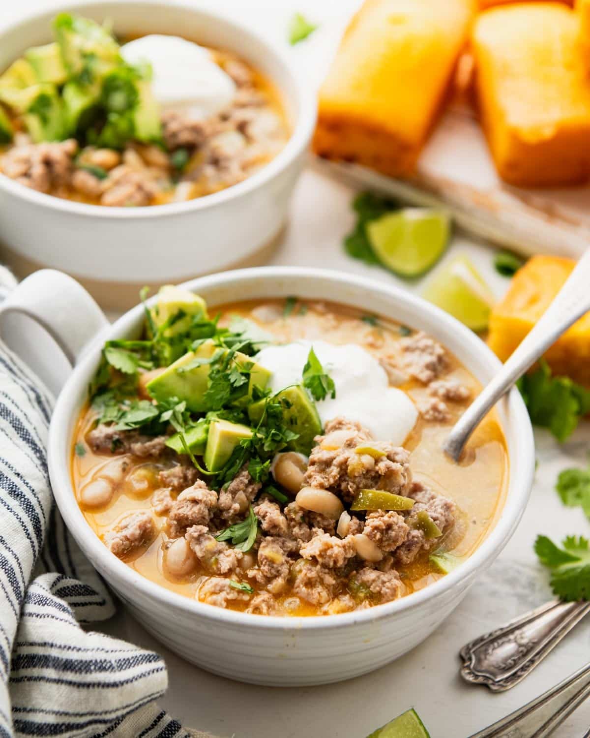 Side shot of two bowls of creamy white turkey chili on a table with a side of cornbread.