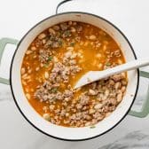 Adding ingredients to a pot of white bean turkey chili.