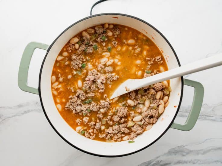 Adding ingredients to a pot of white bean turkey chili.