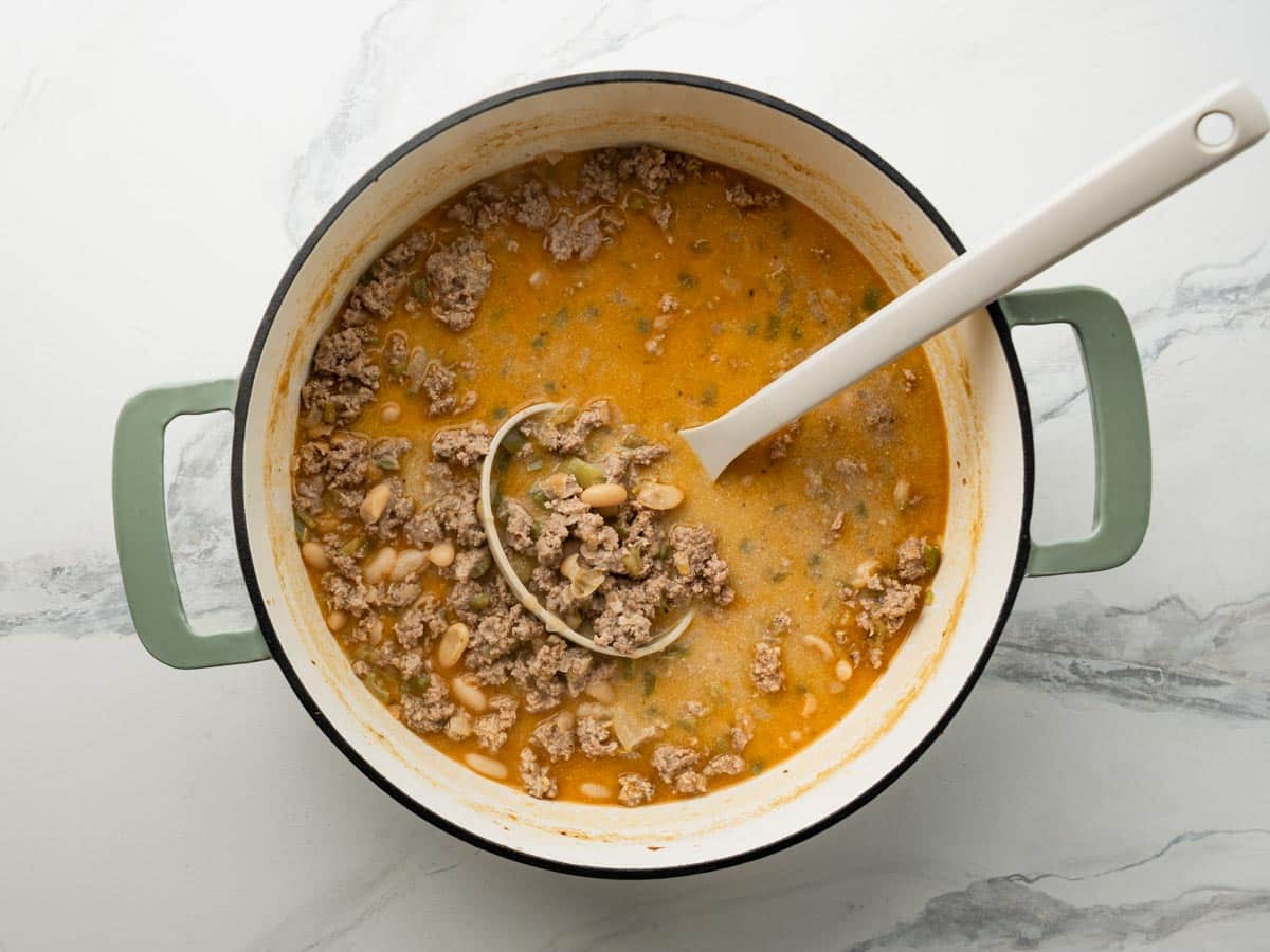 Ladle in a Dutch oven full of creamy white turkey chili.