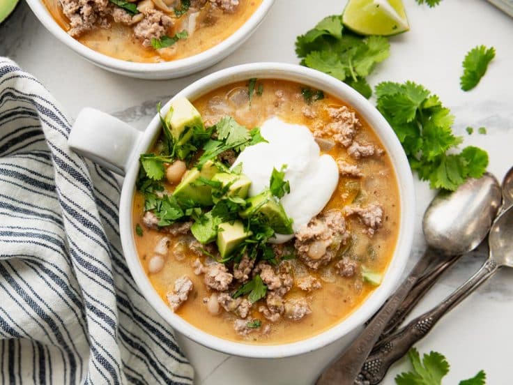 Horizontal overhead image of a bowl of white ground turkey chili with toppings.