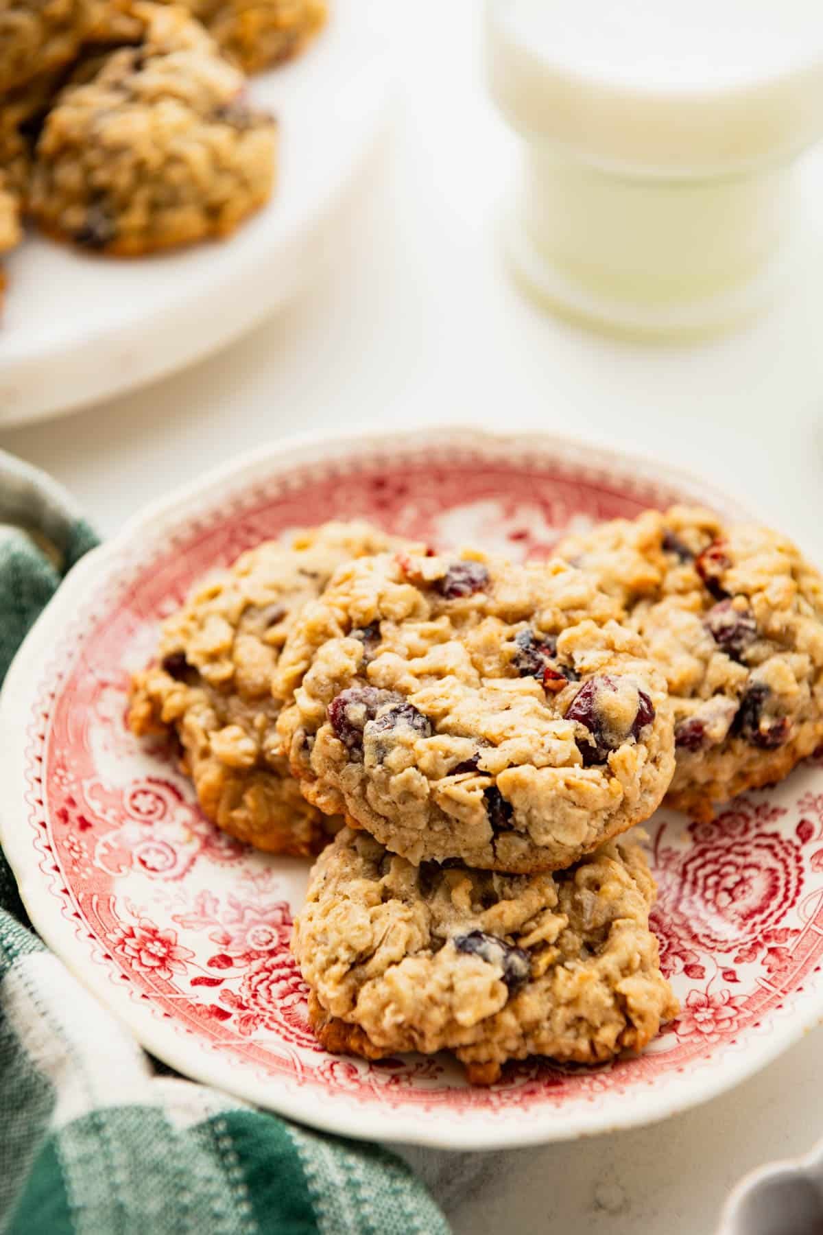 Side shot of chewy oatmeal cranberry cookies on a red and white plate.