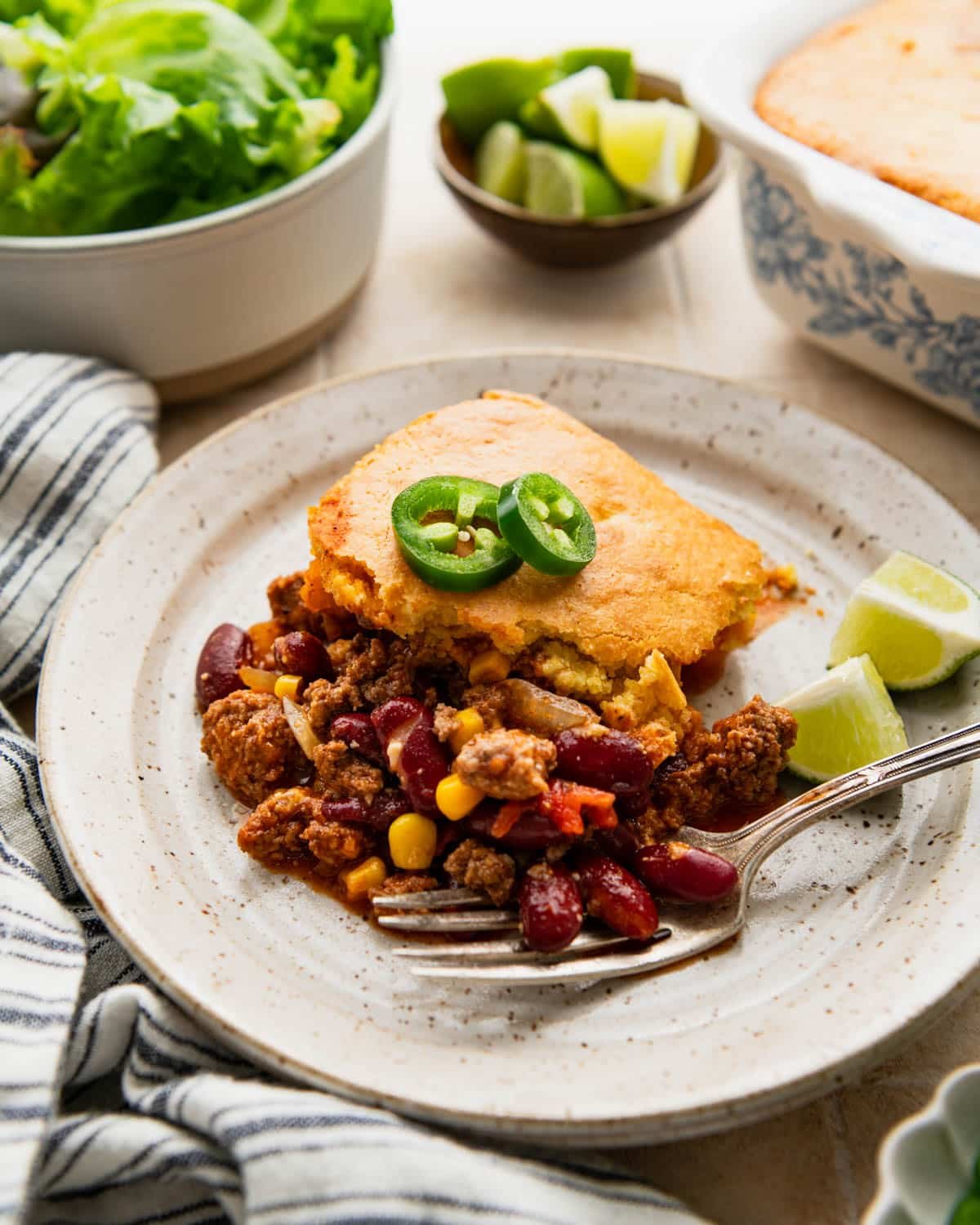 Side shot of chili cornbread casserole on a plate with toppings.