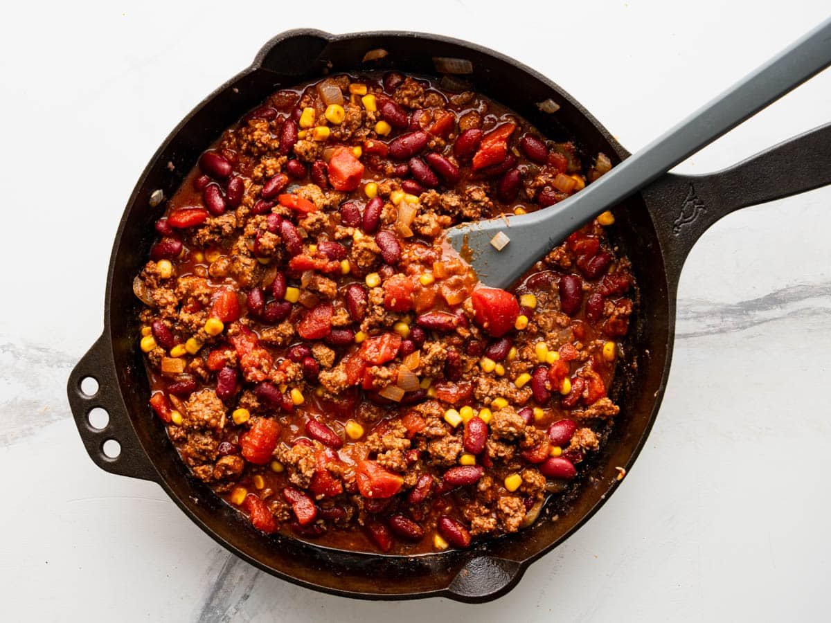 Process shot showing how to make the chili for a casserole in a cast iron skillet.
