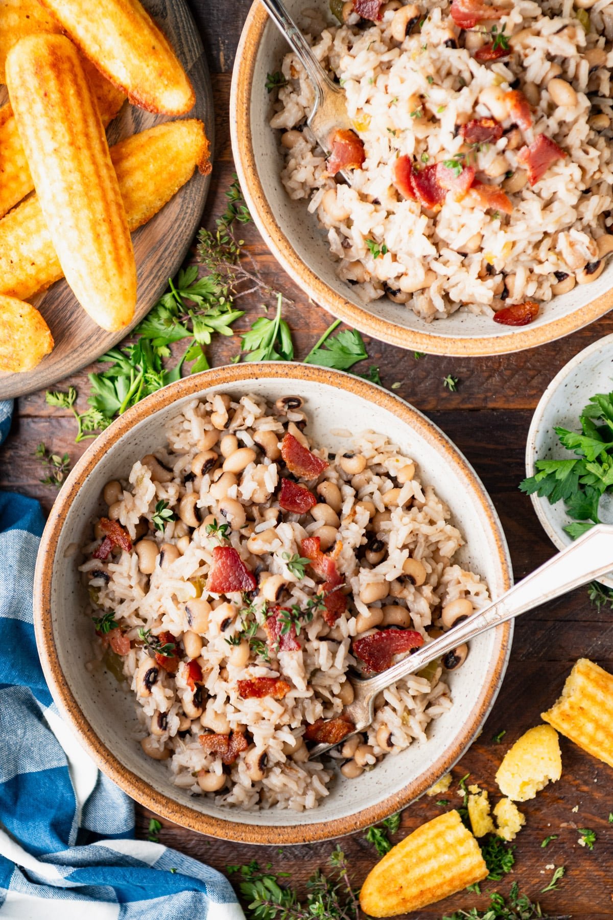 Overhead image of two bowls of Hoppin John on a wooden table with a side of cornbread.
