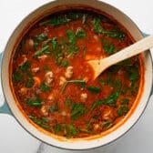 Horizontal overhead shot of adding the spinach to a pot of meatball soup.