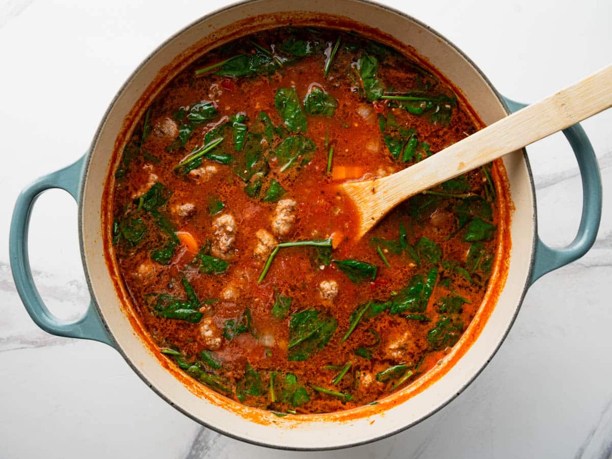 Horizontal overhead shot of adding the spinach to a pot of meatball soup.