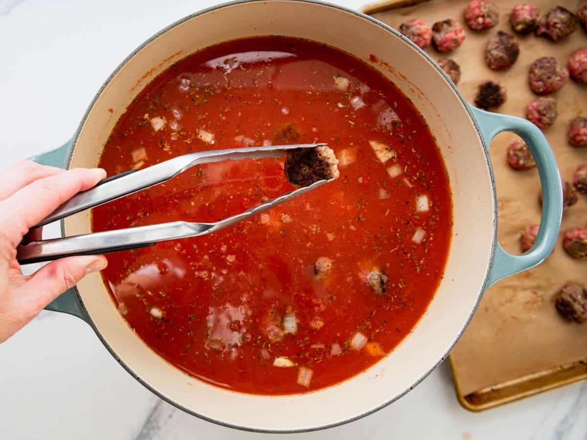 Adding the meatballs back to a pot of soup.