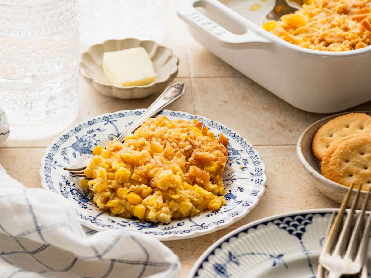 Horizontal side shot of scalloped corn served on a small blue and white plate.