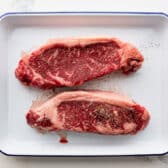 Two strip steaks on a tray.