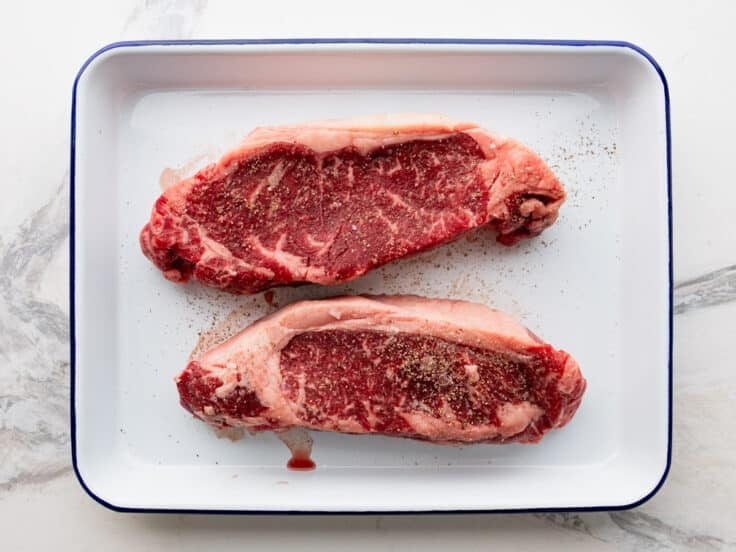 Two strip steaks on a tray.