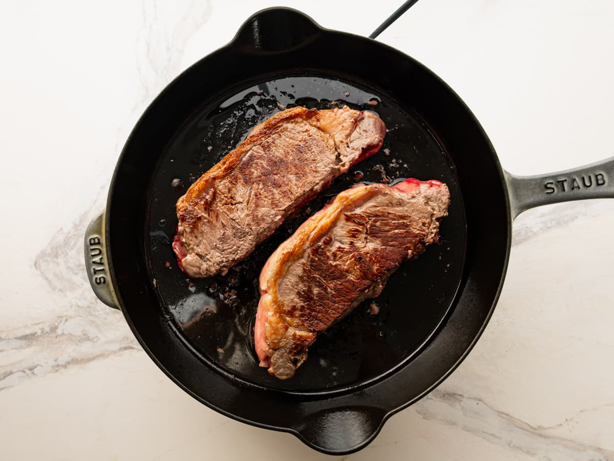Searing New York strip steaks in a cast iron skillet.